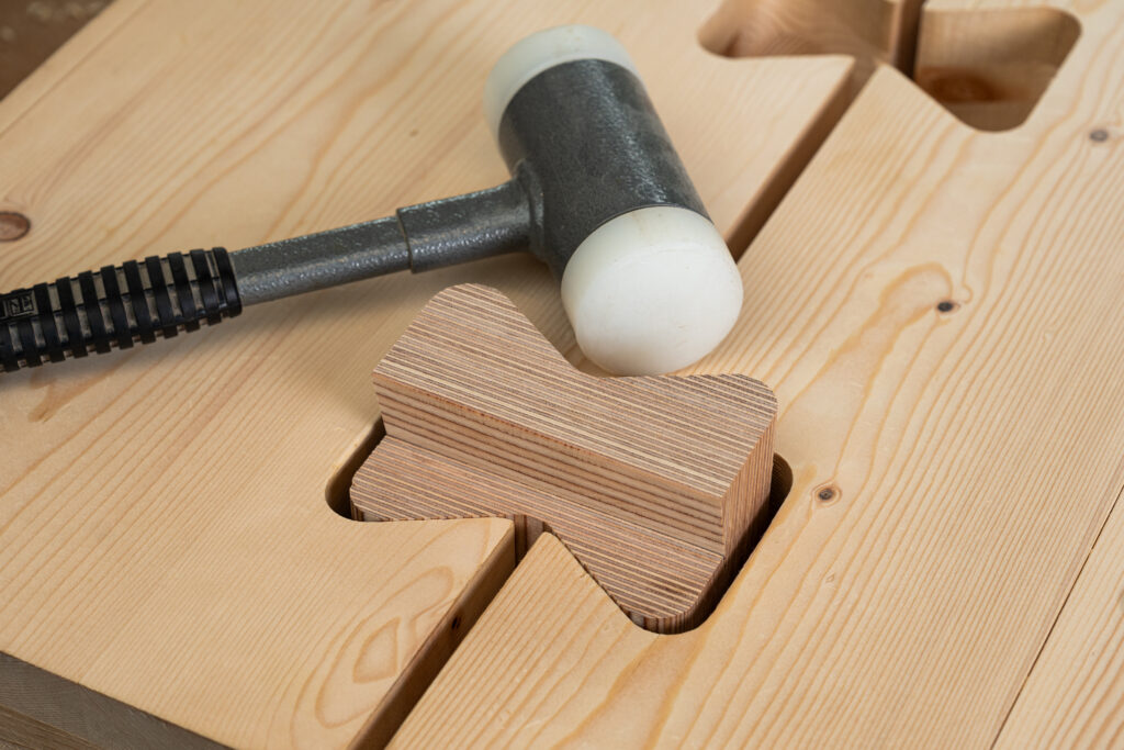 kalapácsal telepítenek egy X-fix pillangó vagy fecskefark stílusú kötőelemek CLT födémbe